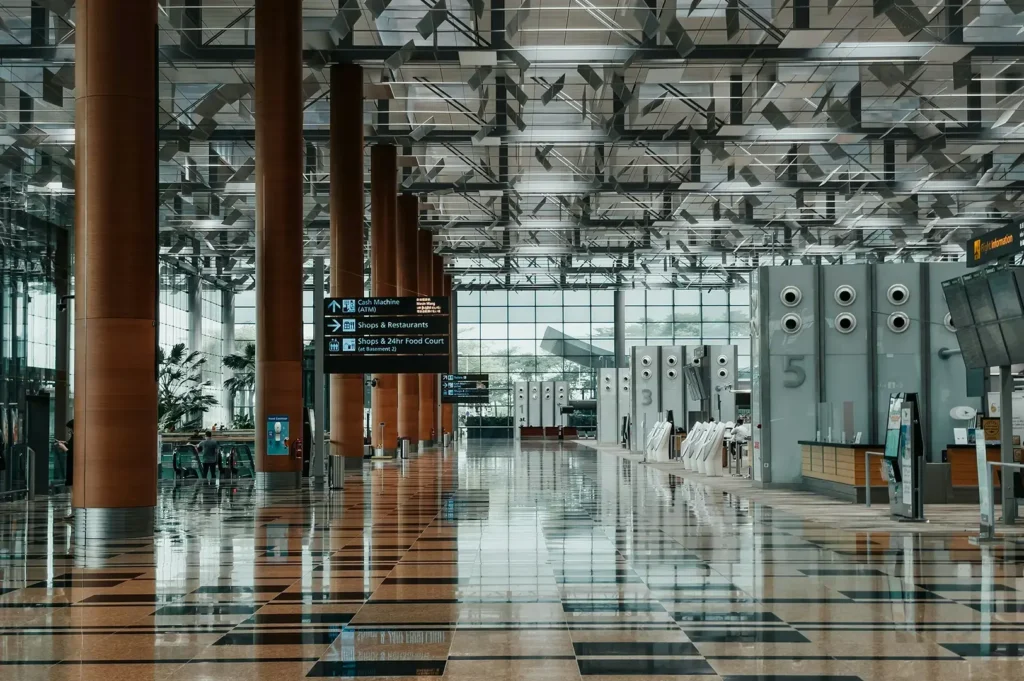Spacious, modern airport terminal interior with high ceilings, wooden pillars, and polished tiled floors.