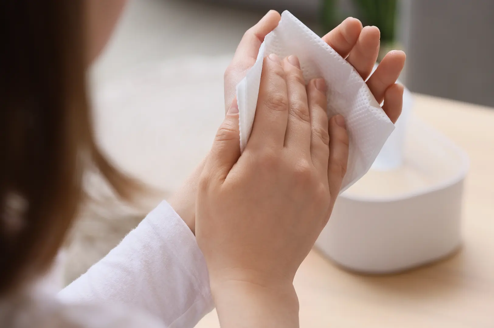 Close-up of hands drying with a white paper towel on a wooden surface.