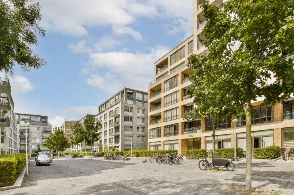 Modern apartment buildings with balconies and large windows line a paved courtyard with parked bicycles and a car.
